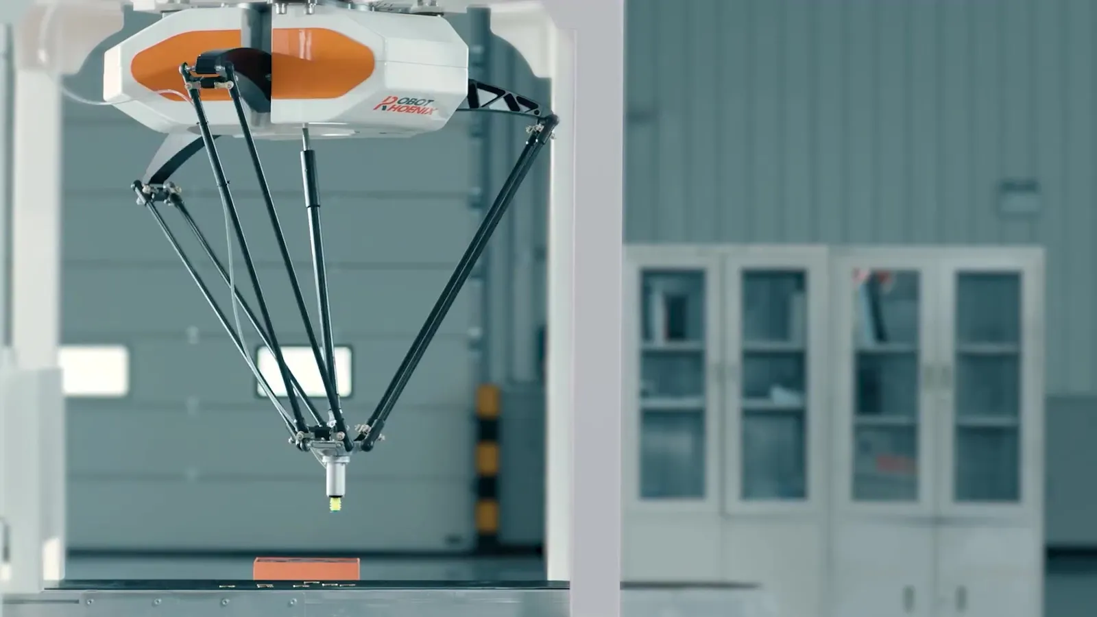 天井から吊られたパラレルリンク（Delta）ロボットが、コンベヤ上のワークに向かう様子